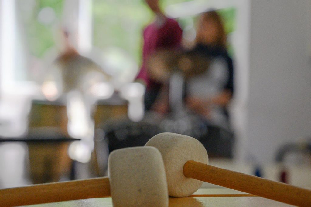 Filzschlägel auf Klangstäben; im Hintergrund zwei musizierende Menschen.